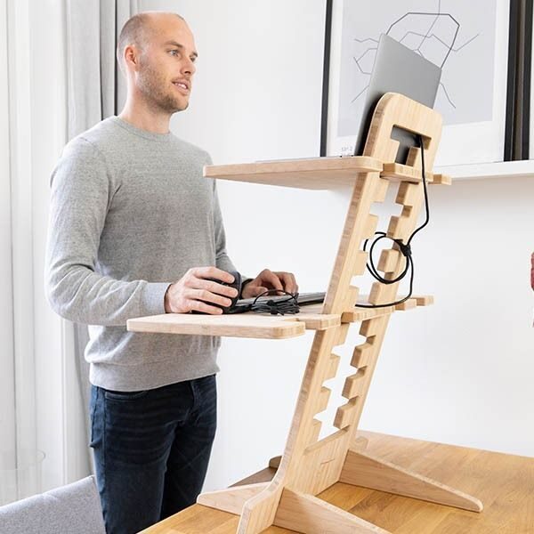 Man gebruikt de OPNIEUW! bamboe zit-sta bureauverhoger op een werkplek met laptop en accessoires