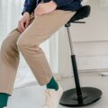Persoon zit op een zwarte Varier Move balanskruk bij een verhoogd bureau, ideaal voor actief zitten en werken